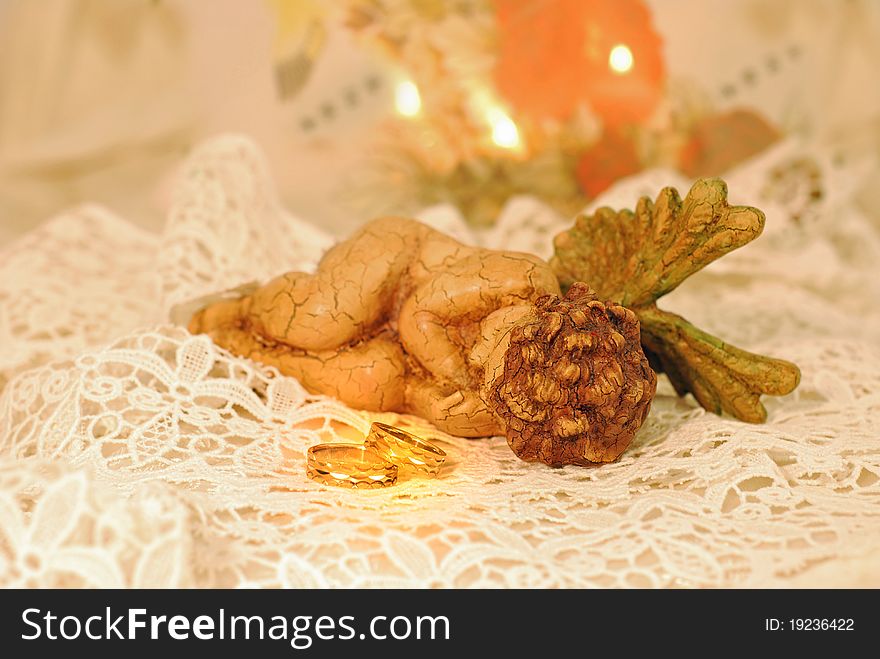 Gold wedding bands on white lace next to an angle. Gold wedding bands on white lace next to an angle