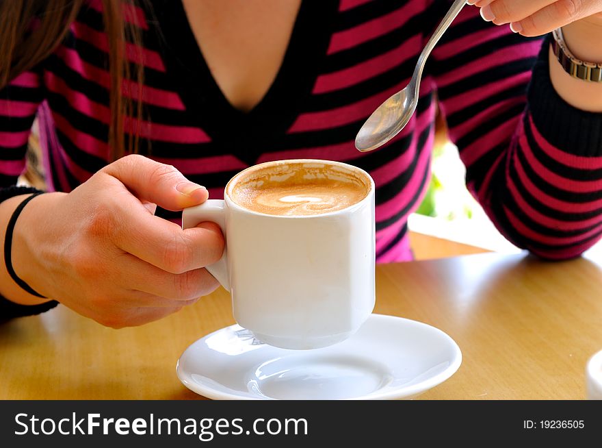 Females holding a cup of cappuccino and a spoon in the other hand. Females holding a cup of cappuccino and a spoon in the other hand