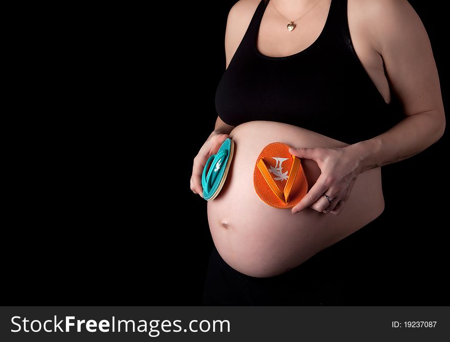 Pregnant woman holding baby sized flip flops. Pregnant woman holding baby sized flip flops