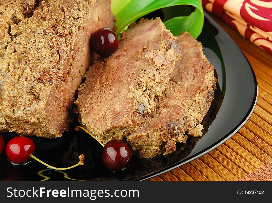 Succulent roast beef meat slices with cherry and leek on a black plate. Succulent roast beef meat slices with cherry and leek on a black plate
