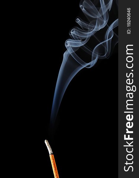 A burning incense stick with white smoke on a black background. A burning incense stick with white smoke on a black background