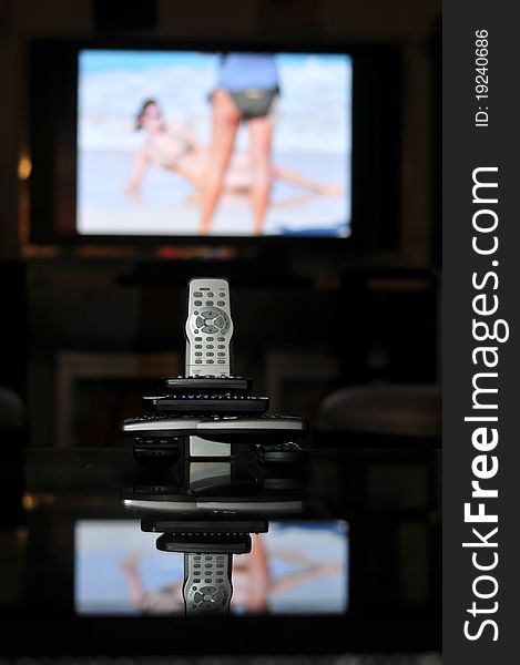 Remote controls for TV on a table in front of a large screen TV. Remote controls for TV on a table in front of a large screen TV