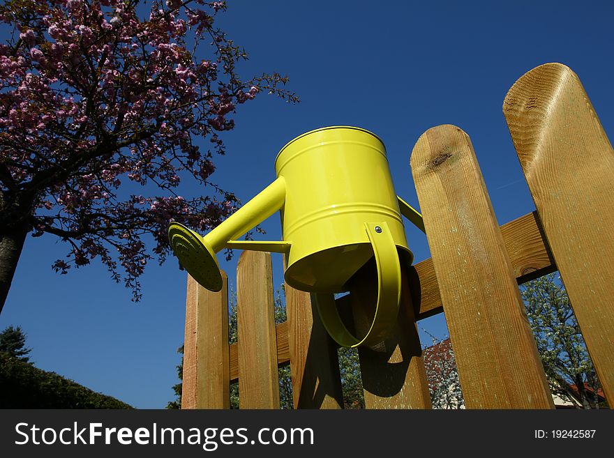 Yellow watering can put-on a wooden fence