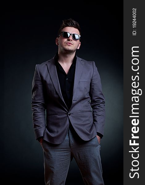 Fashion picture of a man with sunglasses standing on a dark background