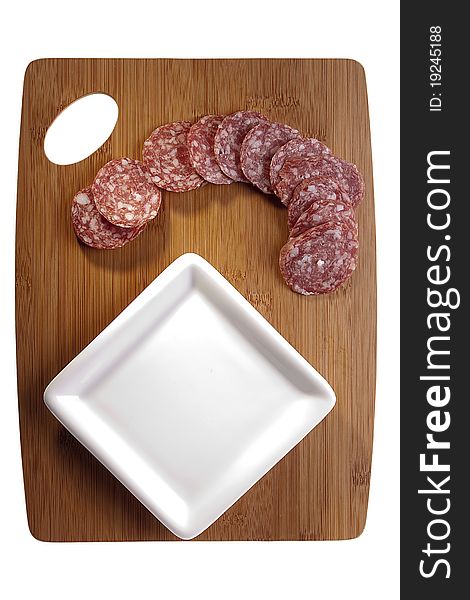 Sliced salami laying next to a white plate on a cutting board.