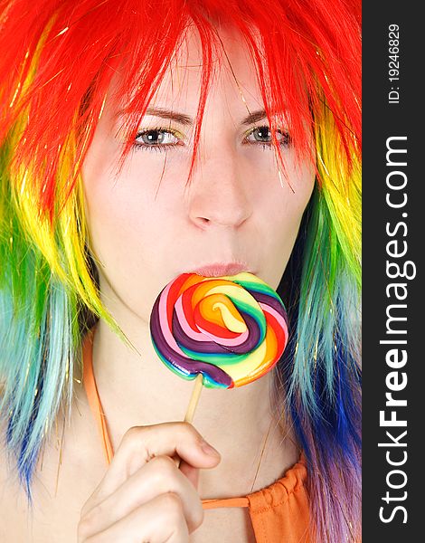 Closeup of young beauty woman in multicolored wig eating big lollipop