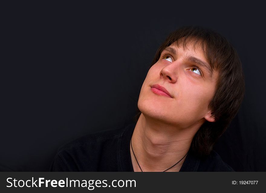 A young guy looks up dreaming on a dark background