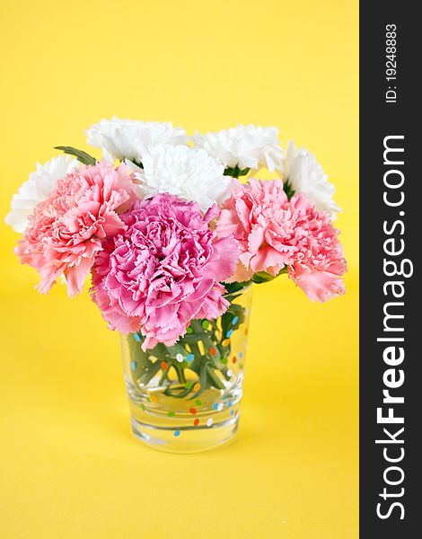 Bunch of flowers: white chrysanthemum and pink carnations (Dianthus caryophyllus‎) in a vase on yellow background