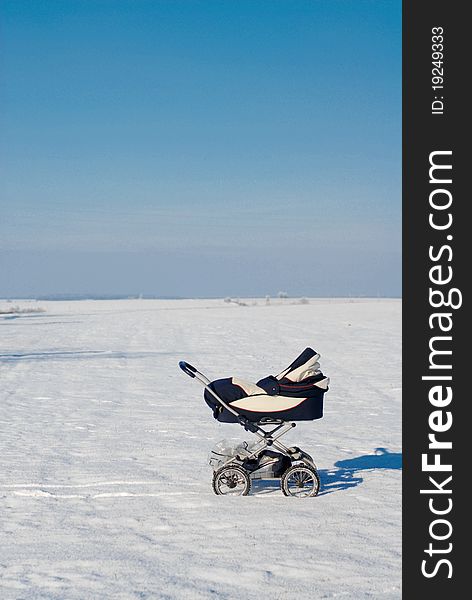 A baby buggy standing alone in the snowy fields under blue peacefull sky. A baby buggy standing alone in the snowy fields under blue peacefull sky.