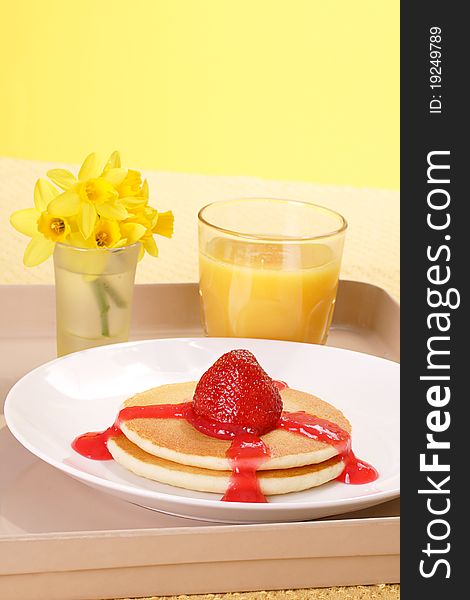 Pancakes garnished with a strawberry and thick coulis and glass or orange juice. Pancakes garnished with a strawberry and thick coulis and glass or orange juice