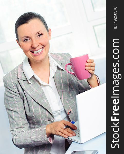 Smiling young business woman with cup using laptop