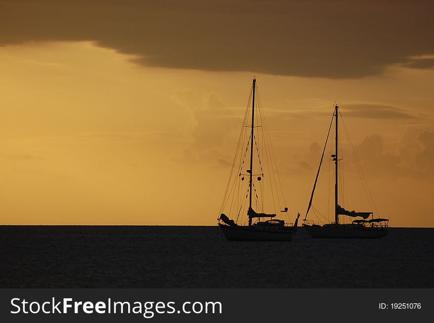 Two sailboats sit in calm waters at sunset. Two sailboats sit in calm waters at sunset.