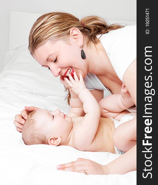 Young  mother and her six months old baby on the bed at home. Young  mother and her six months old baby on the bed at home