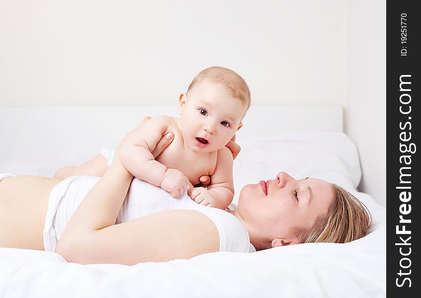 Young mother and her six months old baby on the bed at home. Young mother and her six months old baby on the bed at home