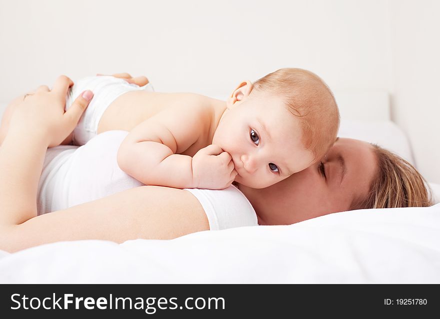 Young  mother and her six months old baby on the bed at home. Young  mother and her six months old baby on the bed at home