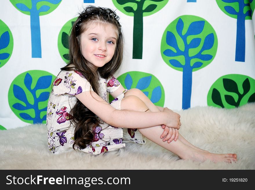 Little girl with long hair in colorful dress sits on the fur on funny tree background