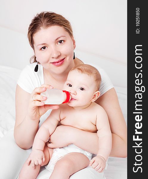 Young mother feeding her her six months old baby with milk  on the bed at home. Young mother feeding her her six months old baby with milk  on the bed at home