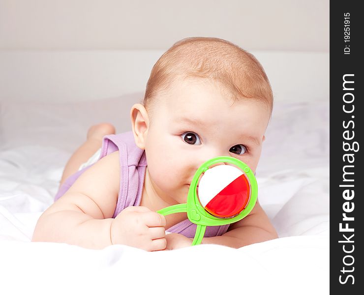 Cute six months old baby on the bed with a toy