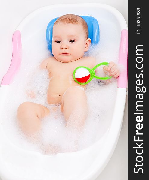 Cute six months old baby taking a bath with foam and playing with a toy