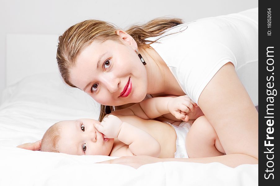 Young  mother and her six months old baby on the bed at home (focus on the baby). Young  mother and her six months old baby on the bed at home (focus on the baby)