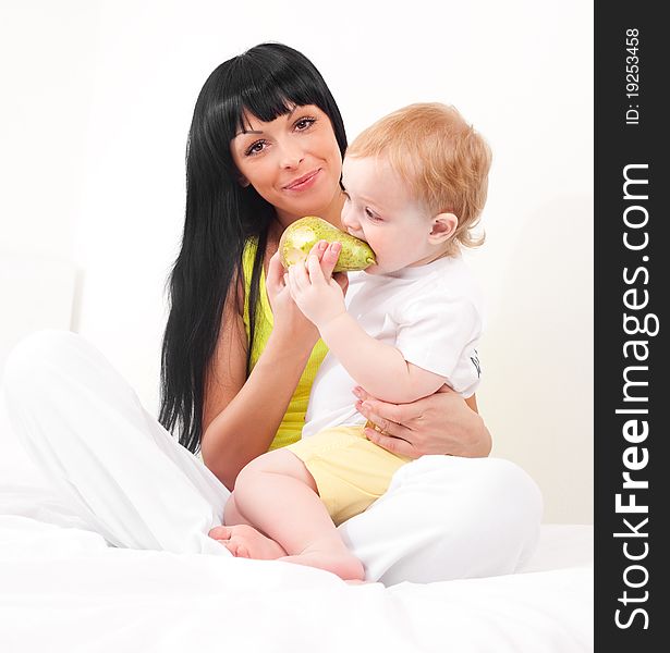 Happy young mother feeding her baby with fruit  on the bed at home. Happy young mother feeding her baby with fruit  on the bed at home