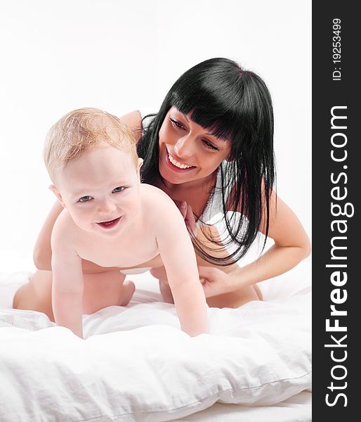 Happy young mother and her baby on the bed at home (focus on the baby). Happy young mother and her baby on the bed at home (focus on the baby)