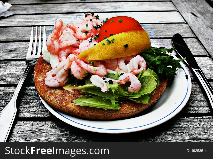 Food on a plate; shrimp sandwich with salad, tomato and lemon.