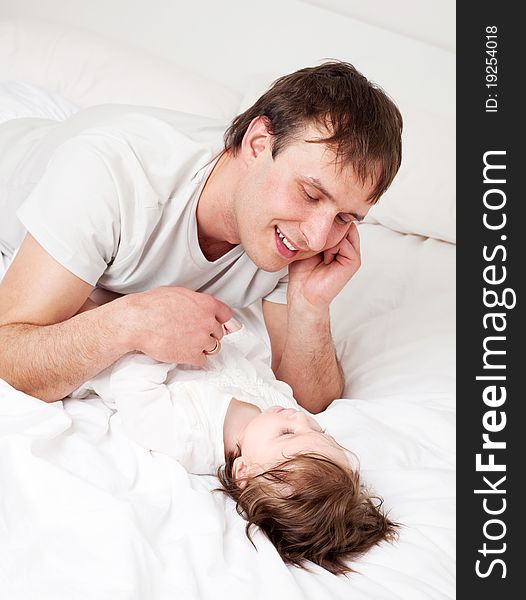 Young father with his six months old daughter on the bed at home (focus on the man). Young father with his six months old daughter on the bed at home (focus on the man)