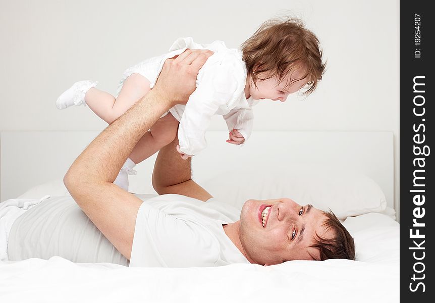 Young father with his six months old daughter on the bed at home (focus on the man). Young father with his six months old daughter on the bed at home (focus on the man)