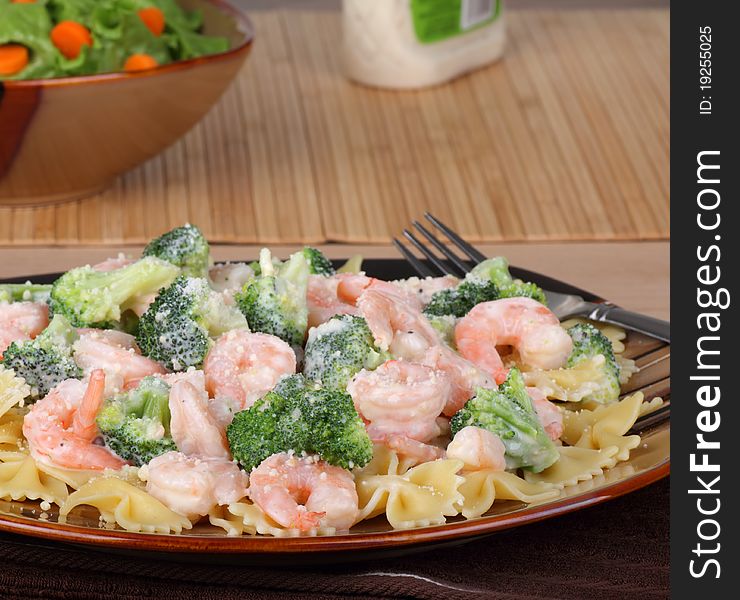 Shrimp, pasta and broccoli with a sauce on a plate with a salad in background. Shrimp, pasta and broccoli with a sauce on a plate with a salad in background