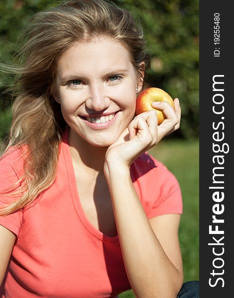 Beautiful young girl smiles happily with apple and beautiful white healthy teeth on the green grass on a sunny day