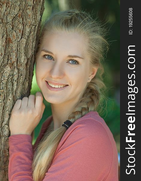 Portrait of a young girl in a park with a romantic smile with blond hair, braided in a braid. Portrait of a young girl in a park with a romantic smile with blond hair, braided in a braid
