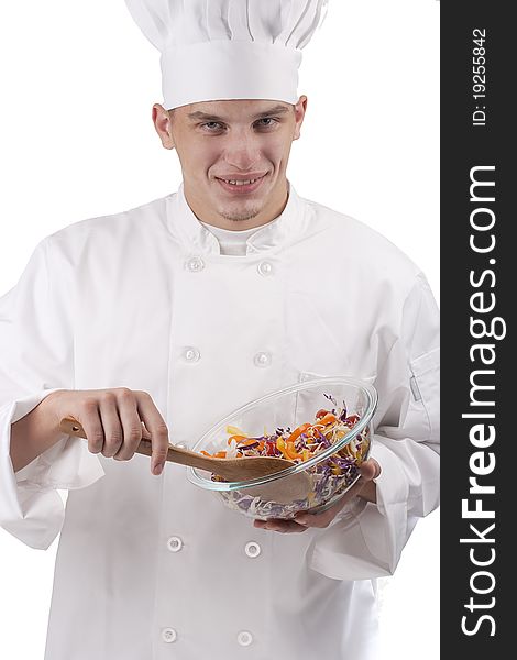 The young chef in uniform and chef's hat in the bowl of salad mixes.