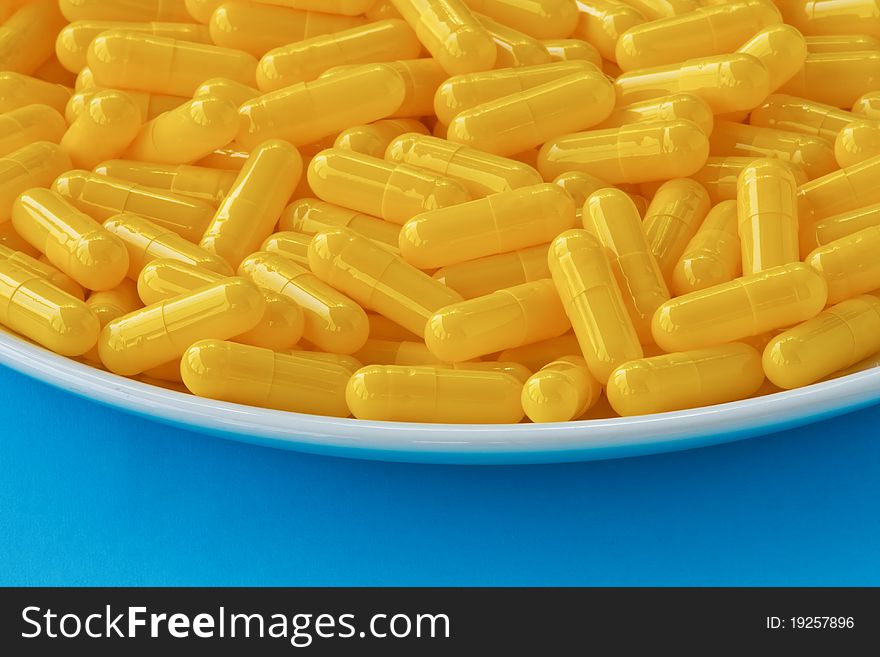 Yellow capsule pills on a white plate on blue black ground. Yellow capsule pills on a white plate on blue black ground