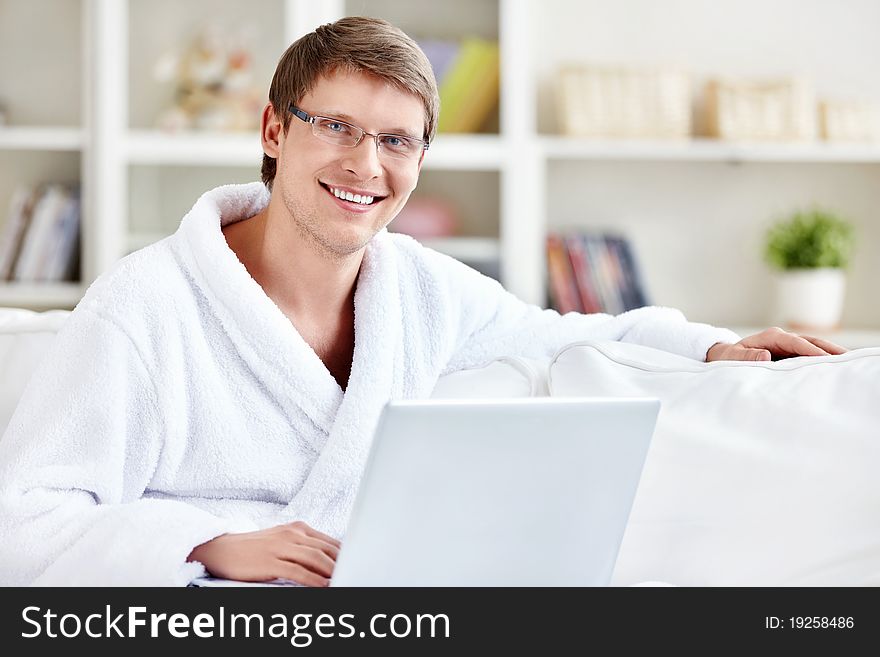 A man in a robe with a laptop at home. A man in a robe with a laptop at home