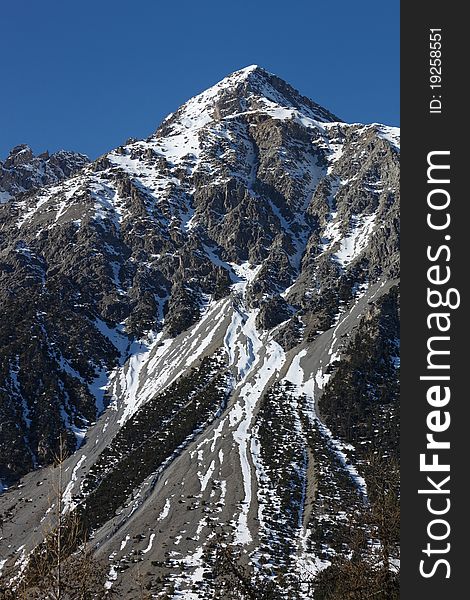 Big mountain peak on the blue sky with the risk of avalanches