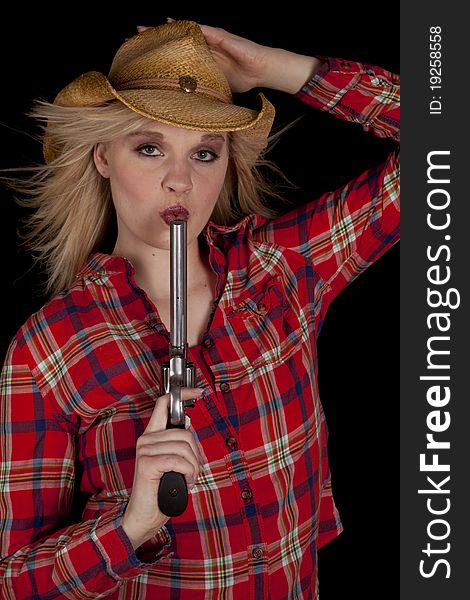 A cowgirl on a black background holding on to her hat while blowing on a pistols barrel. A cowgirl on a black background holding on to her hat while blowing on a pistols barrel.