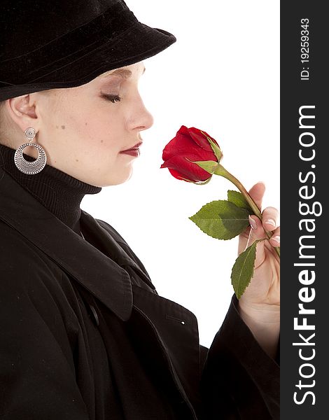A side view of a girl in a black coat and hat smelling a red rose. A side view of a girl in a black coat and hat smelling a red rose.