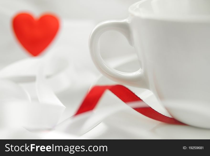 Romantic background with white cup and defocused red heart. Soft focus. Romantic background with white cup and defocused red heart. Soft focus