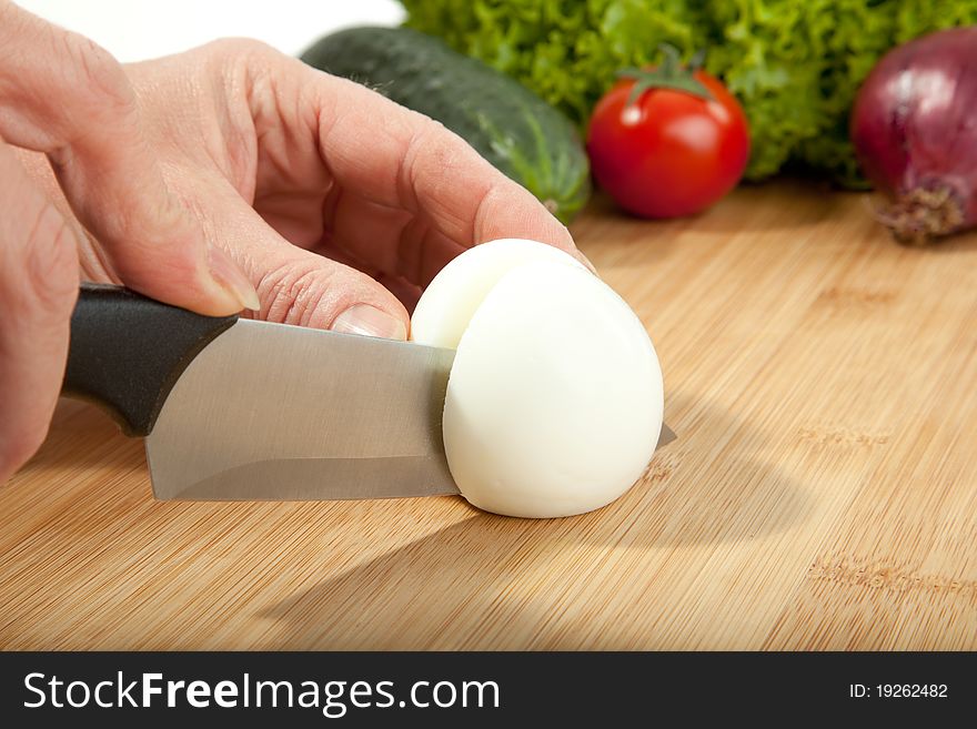 A woman is cutting an egg in preparation for a salad. A woman is cutting an egg in preparation for a salad.