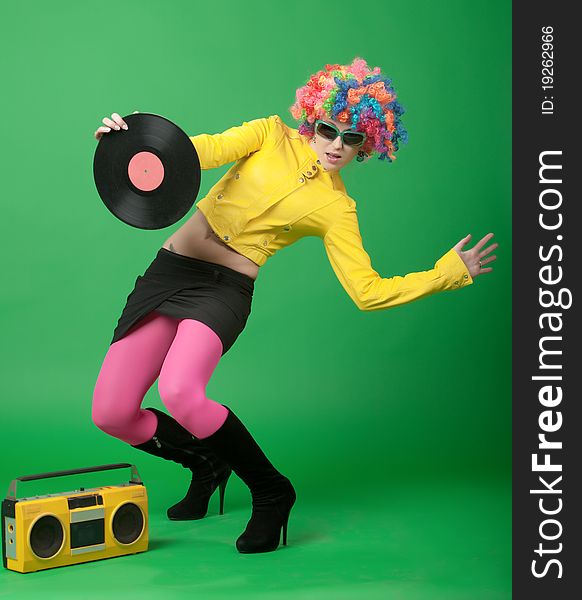 The girl in a color wig with a disk the old tape recorder on green background. The girl in a color wig with a disk the old tape recorder on green background