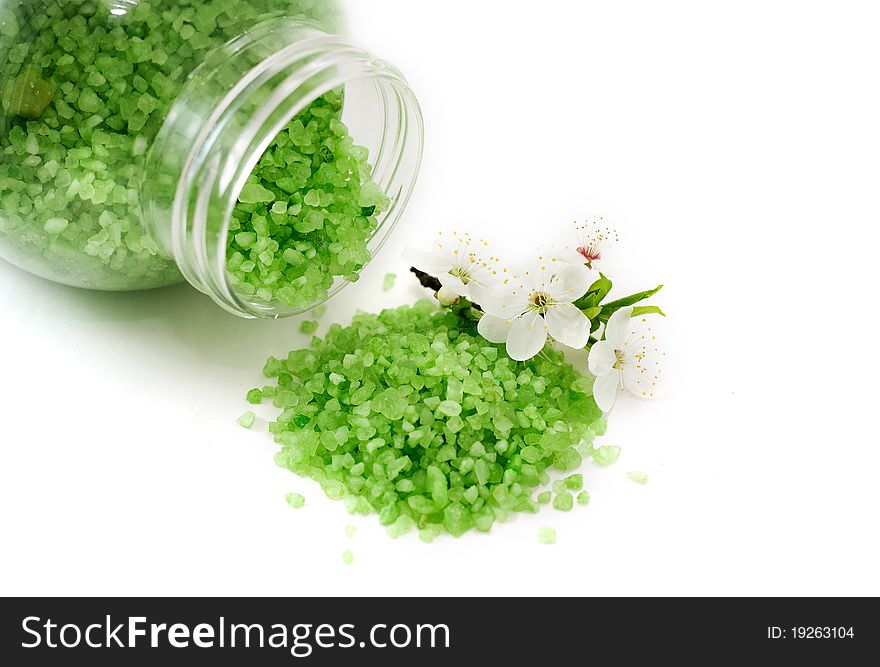 A bottle of bath salt with minerals and a small pink flower lying on white ground