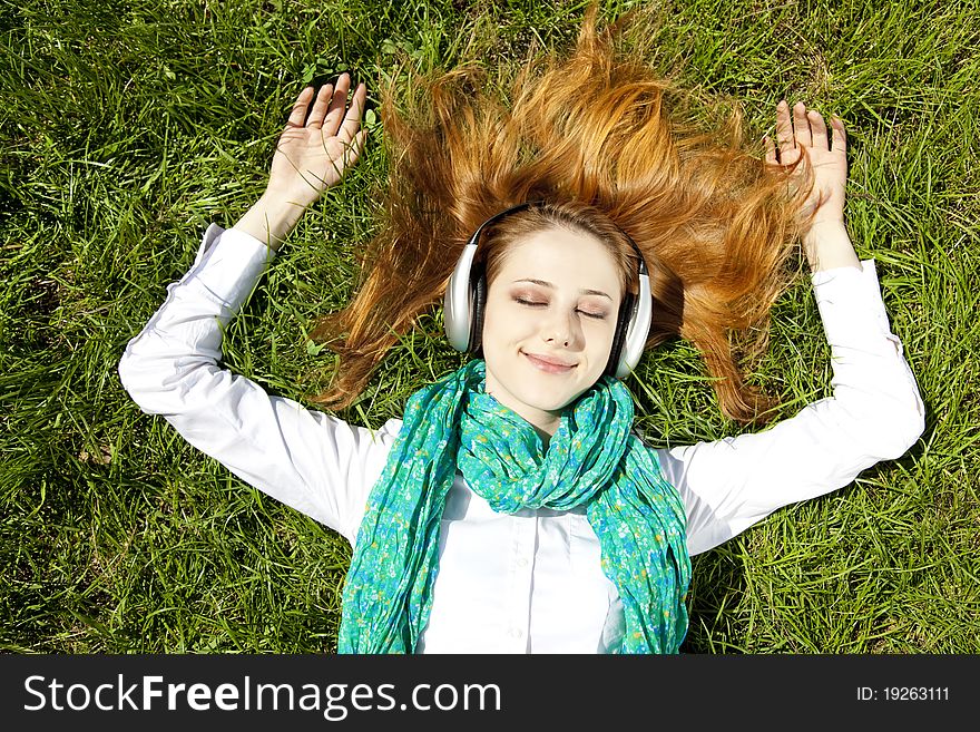 Redhead girl with headphone lies in the park.