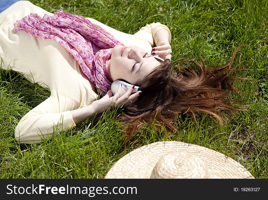 Brunette girl with headphone lies in the park.