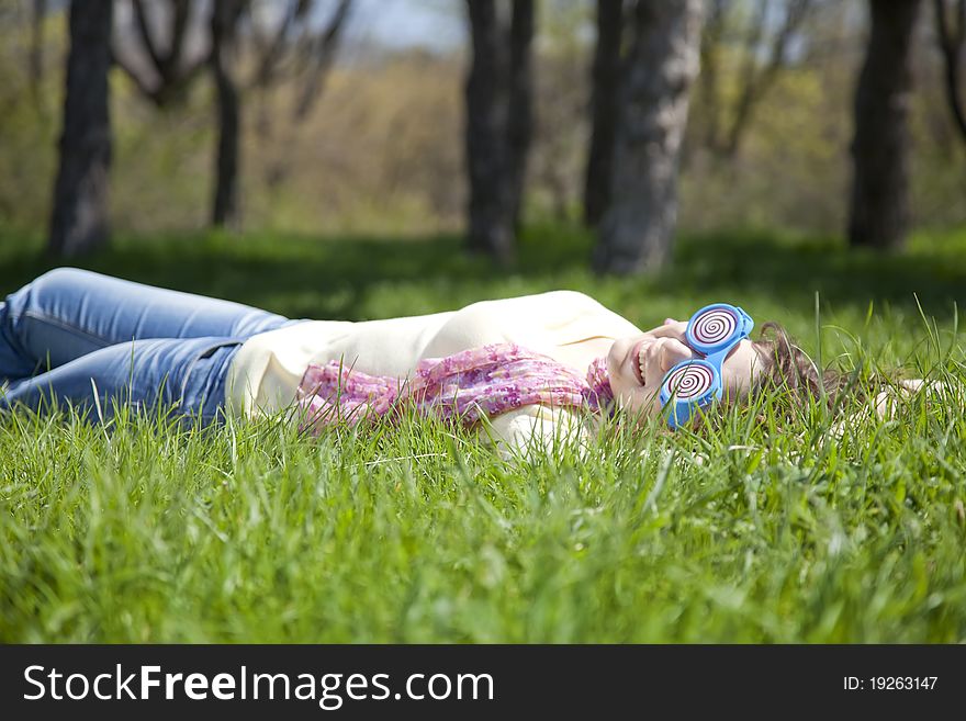 Brunette girl in funny glasses lies at meadow.