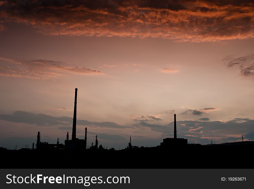 Silouethe of an oil factory with two chimneys, under a dramatic orange sky, photographed at dusk. Silouethe of an oil factory with two chimneys, under a dramatic orange sky, photographed at dusk.