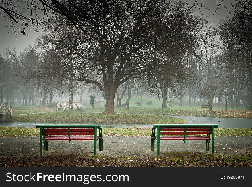 Autumn morning scene of two lonely red benches in an empty misty park. Autumn morning scene of two lonely red benches in an empty misty park.