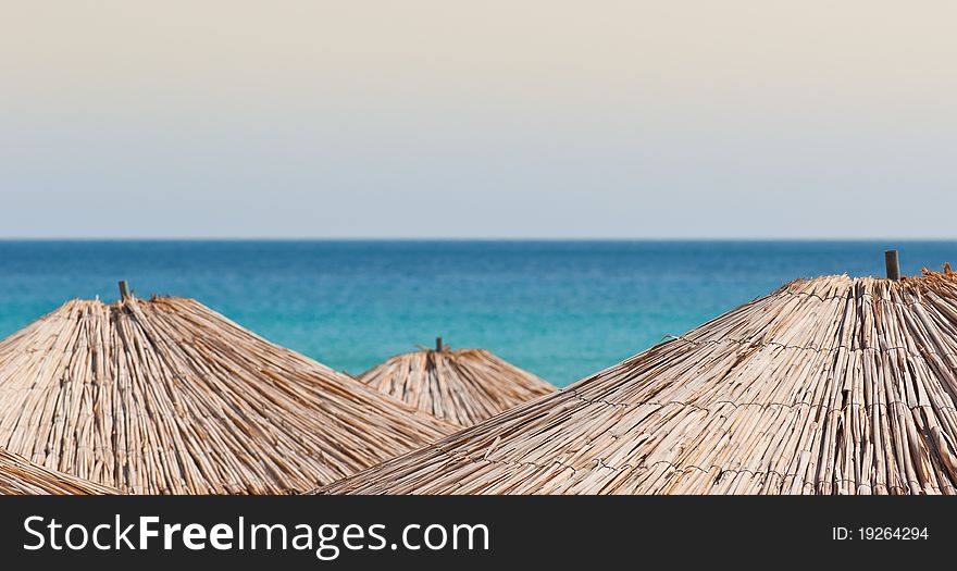 An abstract composition consisting of three straw sun umbrellas. The sea is blured in the background. Shallow depth of field.