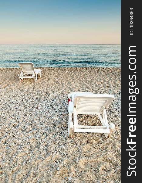 Two white sunbeds on an empty sandy beach at dusk. Two white sunbeds on an empty sandy beach at dusk.