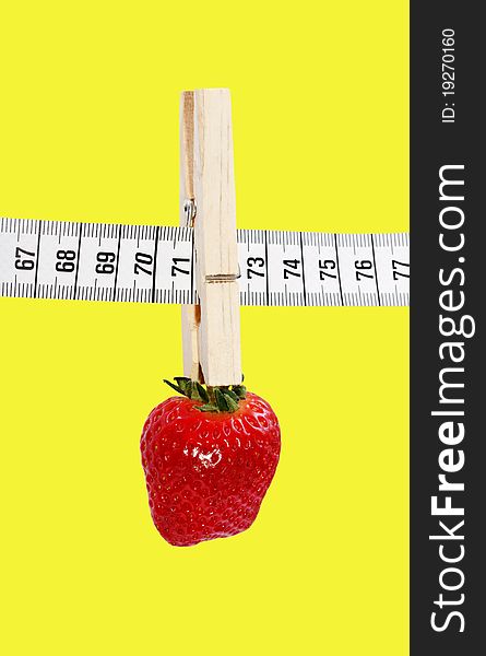 One strawberry hanging on the measuring tape with clothespin isolated on a yellow surface. One strawberry hanging on the measuring tape with clothespin isolated on a yellow surface.